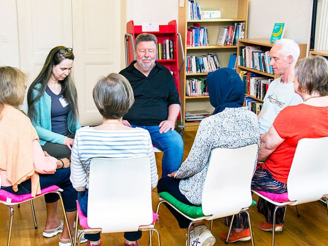 A group of seven Centrepoint members sitting in a circle with their eyes shut meditating