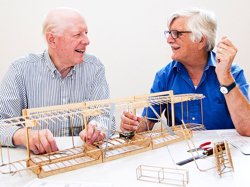 Two men laughing together while working on building a model airplane