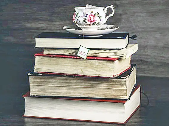 A pile of five hardback books with a bone china floral cup of tea on top
