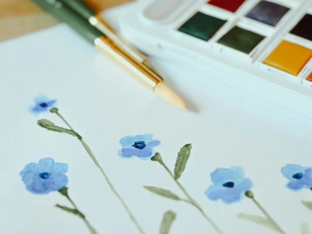 Watercolour painting of blue poppies with two paint brushes and the edge of a paint palette