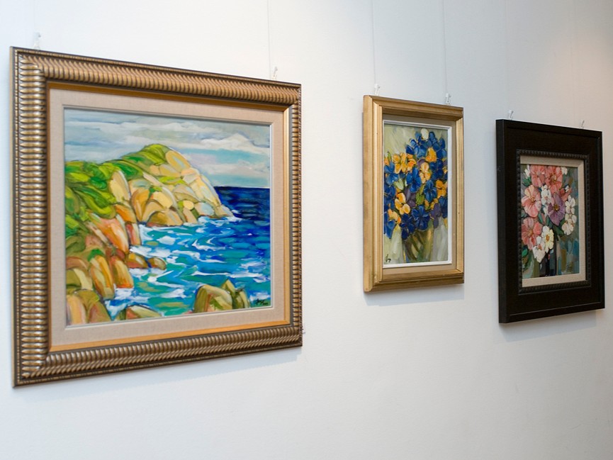 Three paintings hanging on Centrepoint's artwall. Two are of flowers and one is of cliffs by the sea