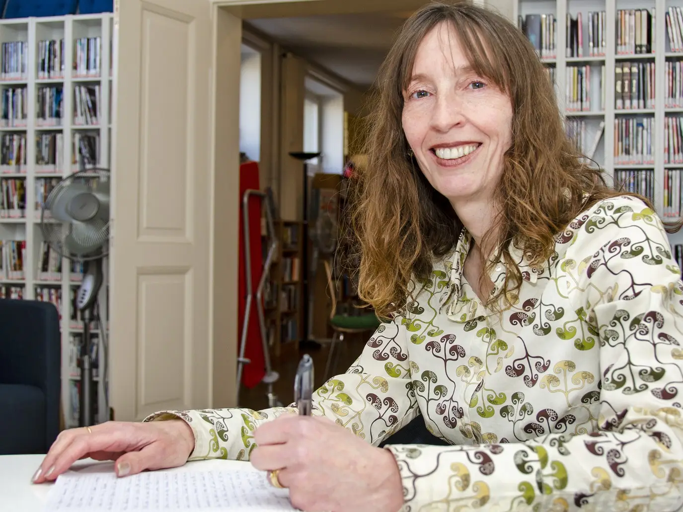 A Centrepoint volunteer smiling at the camera while writing some text at a desk